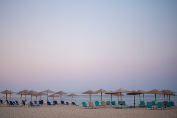 Rows of umbrellas and empty sunbeds on the beach, early in the morning. Nea skioni, Greece. Amazing summer seascape of Adriatic sea. Travel and leisure concepts.