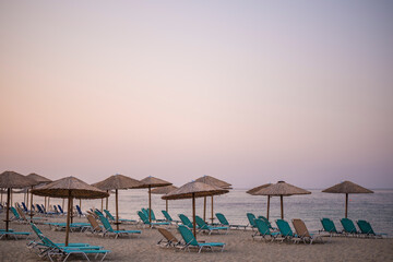 Rows of umbrellas and empty sunbeds on the beach, early in the morning. Nea skioni, Greece. Amazing summer seascape of Adriatic sea. Travel and leisure concepts.