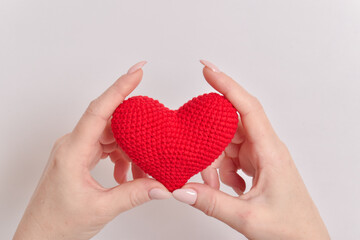 Fototapeta premium A red knitted heart in the hands of a girl with a beautiful manicure. Love. Organ donation. Pregnancy. Valentine's Day.