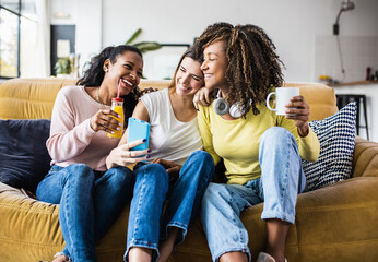 Cheerful multiracial female friends enjoying free time together at home - Three happy young adult...