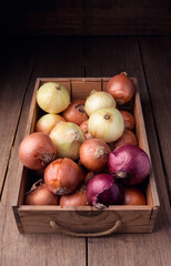 Onions in old box on rustic wooden table, food ingredients
