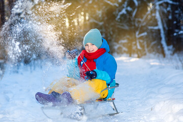 happy boy downhill on a sled in winter. a child in bright clothes sits on a sled