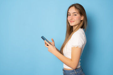 Fototapeta premium Beautiful girl using smartphone standing isolated over blue background.