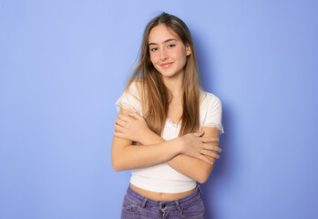 Beautiful young woman in casual clothing hugging herself over purple background. - obrazy, fototapety, plakaty