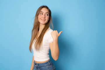 Smiling girl with long hair showing thumb up side and looking away over blue background.