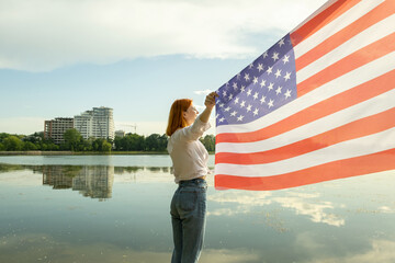 Happy red haired young woman with United States national flag in her hand. Positive girl celebrating US independence day.