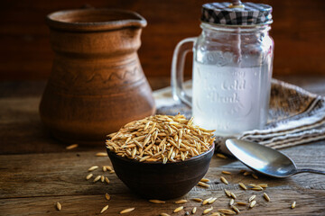 On the wooden kitchen table are a ceramic bowl of oat grains, a glass cup with oat kvass on a...
