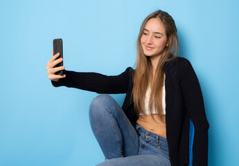 Pretty young happy woman making selfie on smartphone isolated over blue background.