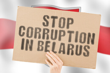 The phrase " Stop Corruption in Belarus " on a banner in men's hand with blurred Belarusian flag on the background. Forbidden. Prevent. Wealth. Offence. Corruptness. Economy. Corruptible. Political