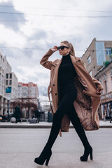 Young beautiful girl in a beige coat and sunglasses walks through the city