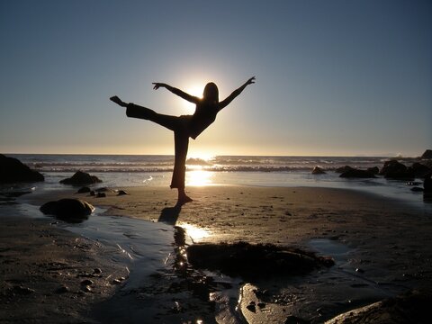 Silhouetted dancer on the beach poses in arabesque in front of the setting sun.