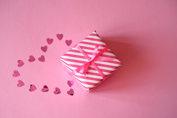 A pink confetti heart is laid out on a background next to a gift box tied with a ribbon with a bow. A valentine's Day gift. Give presents for the holidays