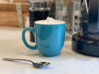Morning cup of coffee with steamed milk foam in teal mug