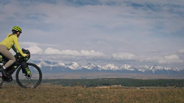 The man and woman travel on mixed terrain cycle touring with bikepacking. The two people journey with bicycle bags. Mountain snow capped.