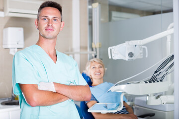 Obraz premium Confident male stomatologist in his clinic with patient in chair behind