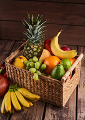 Mix of fresh juicy colorful exotic tropical fruits in basket on wooden background