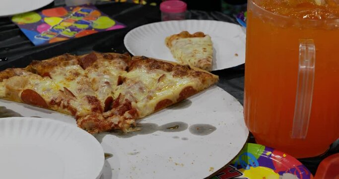 Sad looking leftover kids birthday party event pizza pepperoni and cheese on table as Hispanic Latin person sets pitcher of orange soda down - in Cinema 4k (30fps slowed from 60fps).