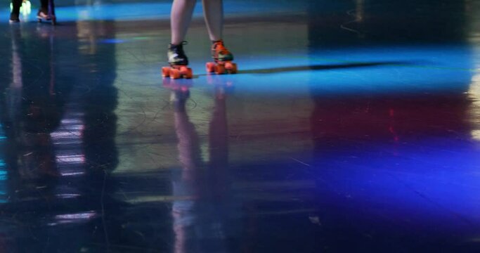 Busy roller skating rink with razor scooters rollerblades and rollerskates on people as they skate around brightly colored darkly lit venue - in Cinema 4k (30fps slowed from 60fps).