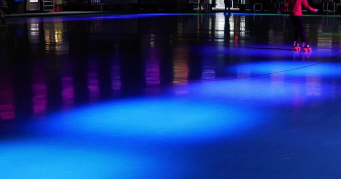 Not very busy roller skating rink with skaters rolling around the brightly colored flashing lights of the event venue - in Cinema 4k (30fps slowed from 60fps).