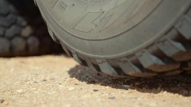 Static low close-up hand held shot of a flat punctured tire suspended above the ground after being jacked up.