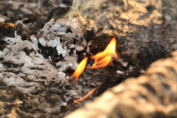 Close-up of a defocused view of a smoldering fire. Blurred background. A small flame of a dying fire, smoke. Cozy warm atmosphere due to outdoor recreation by the fire, burning.