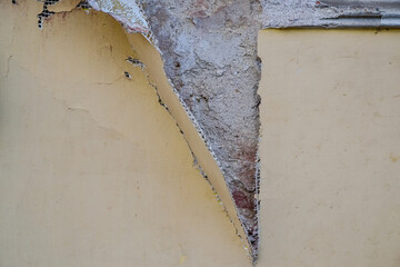 Exterior wall of a building with damaged stucco. Demonstration of poor-quality insulation of buildings. Thin layer of plaster and reinforcing mesh. Construction and repair. Selective focus. Close-up.
