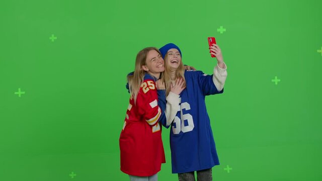 Two girls football fans making selfie. Funny hipster females making self portrait . Young women in spotry clothes having fun in front of green screen background. Chroma key