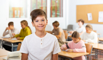 Happy boy stands in a school class against the background of classmates