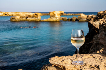 Glass of cold white dry white wine served on rocks in blue sea bay near Protaras touristic town on Cyprus