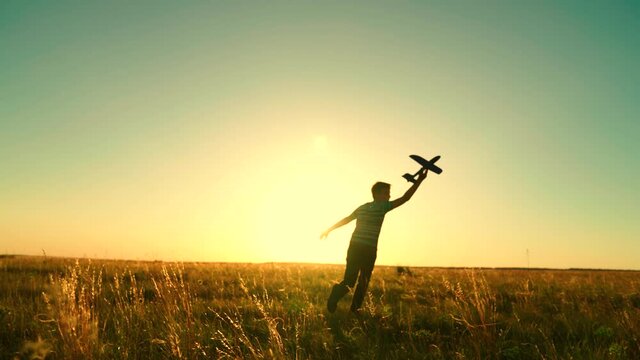 Children's fantasy, the child runs with a toy plane. Silhouette of a happy kid playing with a toy plane at sunset on the field. The boy dreams of becoming an astronaut, an airplane pilot, childhood