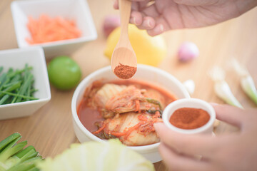 The chef is seasoning kimchi with red chili powder.