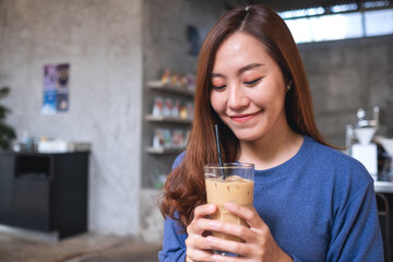 Portrait image of a young asian woman holding and looking at a glass of iced coffee