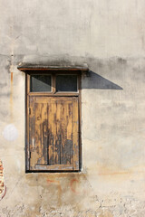 Single window with wooden shutters closed on a concrete wall of an old house.