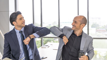 Two male managers greet each other by having elbow bump in the office as a new normal practice...