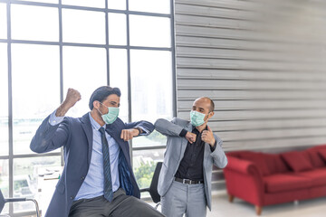 Two male managers with hygienic face masks celebrate their success with elbow bump in the office as a new normal practice during COVID-19 pandemic. New business model to prevent COVID-19