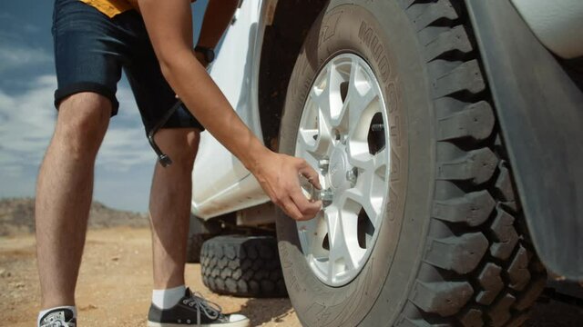 Low angle wide hand held shot of a Caucasian male tourist in Africa as he removes loose a lug nut by hand from a flat tire.