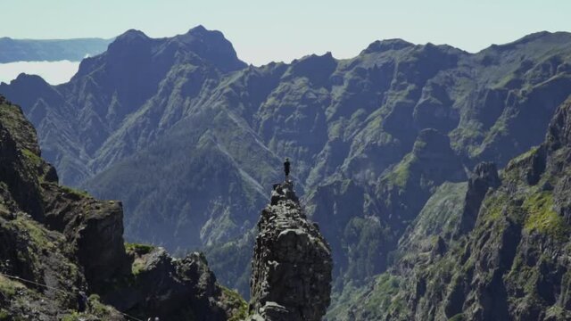 Zooming in to man standing on small rock outcrop overlooking volcanic mountains