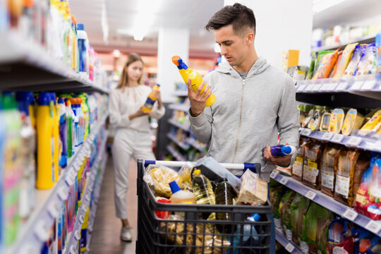 Young glad cheerful smiling male customer making purchases in supermarket, buying household chemicals