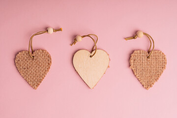 Flat lay of three wooden heart shaped decoration laying on pink background in a row. Concept of love and relationship using for valentine day holiday