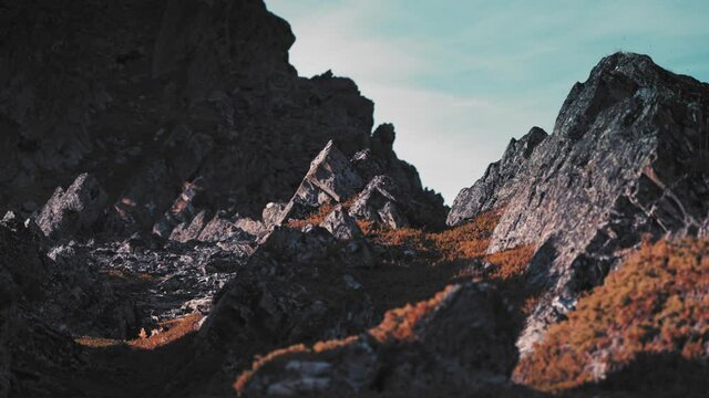 An outlandish landscape of the Varanger coast. Dark crumbling stone formations are covered with patches of reddish moss and dry grass against the pale sky. Slow-motion, pan left.