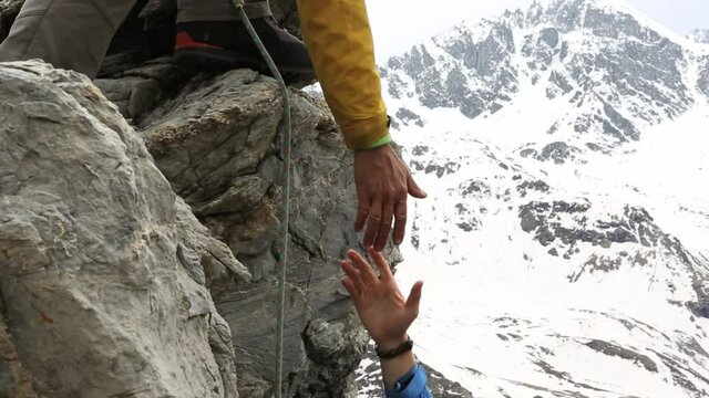 Climbers ascend a rugged rock face with mountains behind