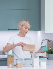 A woman puts things in order in the kitchen, puts food in reusable eco-friendly containers. Pretty woman organizes healthy eating, placement and sorting in the kitchen.