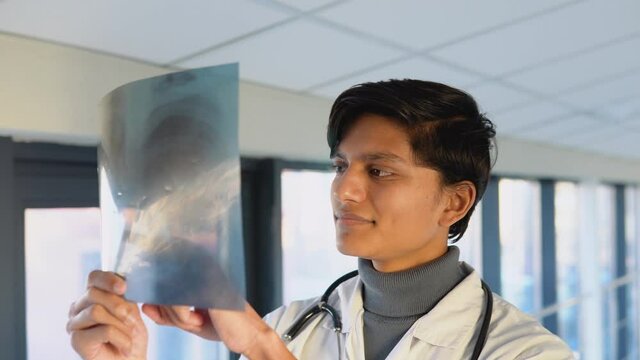 Indian doctor or intern examines x-ray of lungs, holding it in hands indoors. Specialist holds transparent image of chest in arms, and carefully researches it