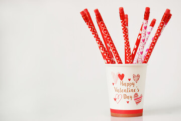 Vaso blanco desechable con lápices de colores adentro. Concepto San Valentín, espacio para texto al lado izquierdo.