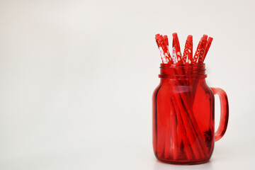 Taza roja de vidrio con lápices adentro, decorados con corazones. Espacio para texto al lado izquierdo.