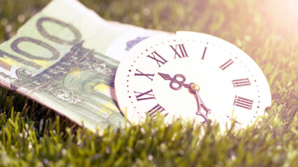 Roman clock and 100 euros on the green grass, summer.