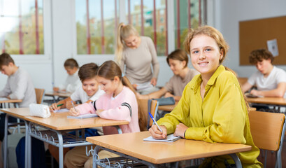 Fototapeta premium Focused teenage students studying in classroom with teacher, writing lectures in workbooks