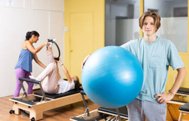 Portrait of teen boy standing with fitness ball during pilates training at gym