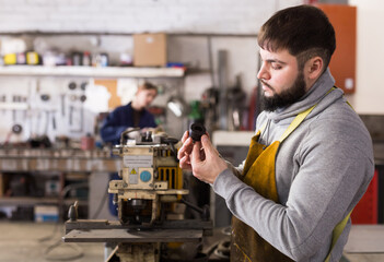 Focused bearded metalworker checking metal part made on vertical milling machine in workshop..