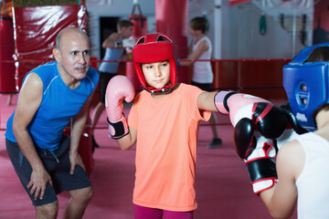 Positive girl teenage sparring at boxing workout with coach on boxing ring